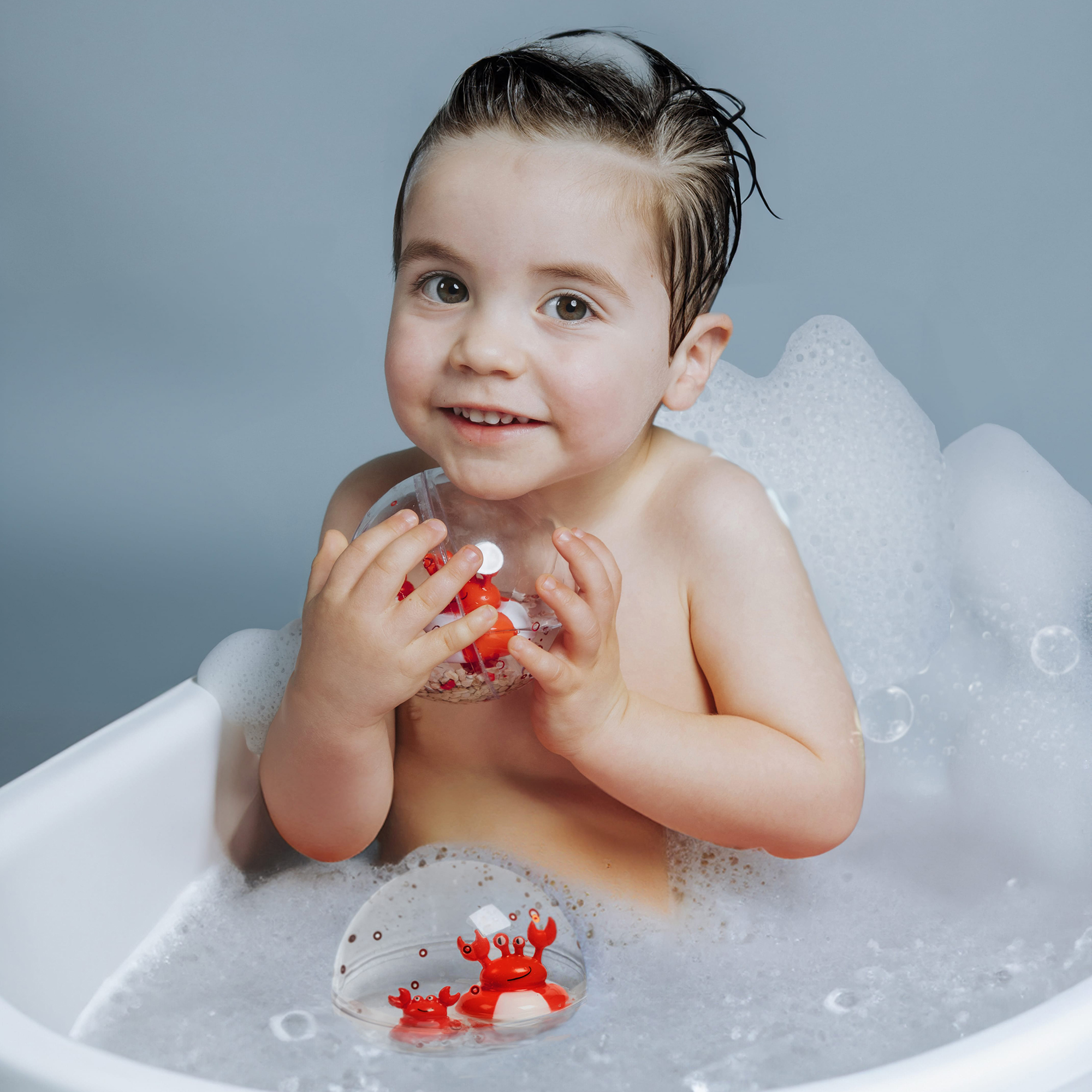 Baby spielt mit Petit Boum Happy Bubbles Sensory Ball während der Badezeit